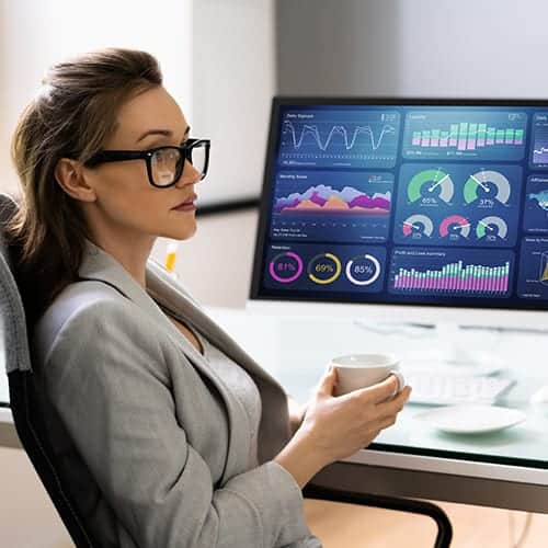 A businesswoman holds a cup against a background of graphs on a desktop screen