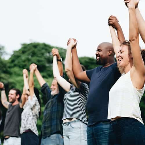 Unifund helps the community to grow stronger together Happy diverse group of people holding hands and raising towards the sky